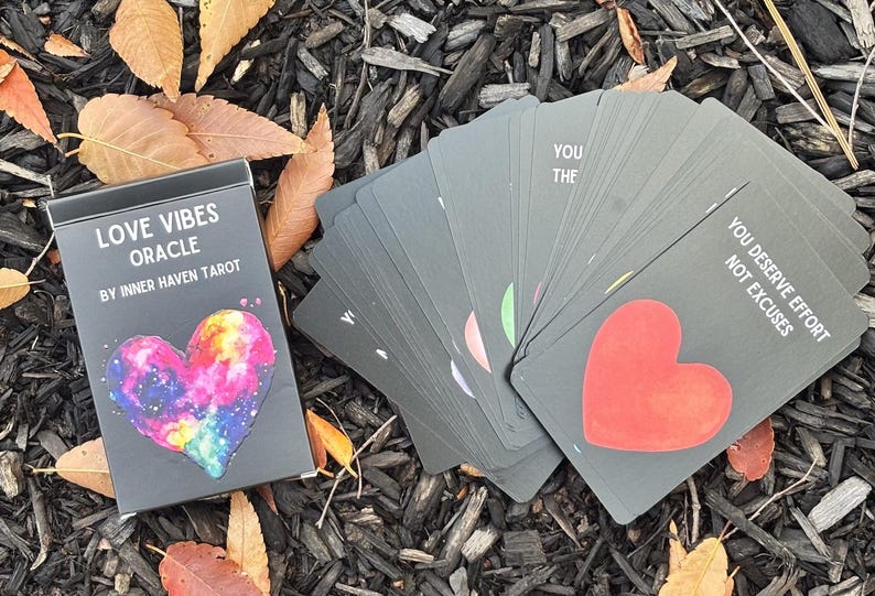 May include: A deck of Love Vibes Oracle cards by Inner Haven Tarot. The black box features a colourful heart design. The cards are grey with a red heart and text that reads "You deserve effort not excuses."