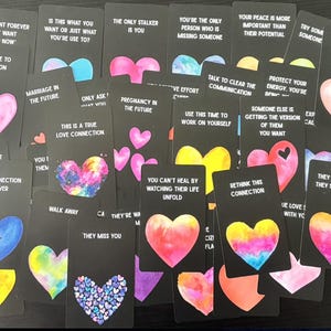 May include: A selection of black tarot cards, each with a colourful heart design and a different phrase. The cards display pink, blue, yellow, and purple hearts, with text such as "Marriage in the Future" and "This is a True Love Connection."