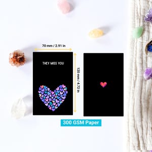 May include: Two black greeting cards, each 70 mm wide and 120 mm tall. One card features a heart made of colorful hearts and the text "THEY MISS YOU". The other card has a small pink heart. The paper is 300 GSM.