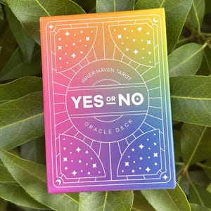 May include: A rectangular oracle deck box featuring a vibrant rainbow gradient background transitioning from orange at the top to purple at the bottom. The front displays white line art of stars and geometric patterns with the text Inner Haven Tarot Yes or No Oracle Deck.