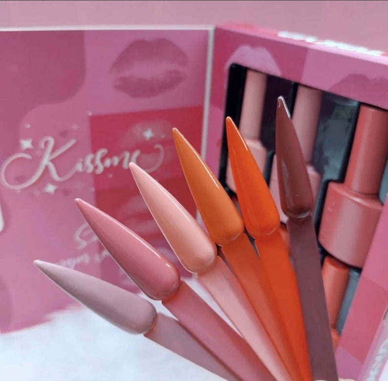 K&ouml;nnte beinhalten: Ein Set mit sechs Nagellackflaschen in Nude-Farben mit dem Wort "Kissme" auf der Schachtel. Die Flaschen sind in einer Reihe angeordnet, wobei die Kappen zum Betrachter zeigen. Die Flaschen sind alle in verschiedenen Nuancen von Nude, von hell bis dunkel.
