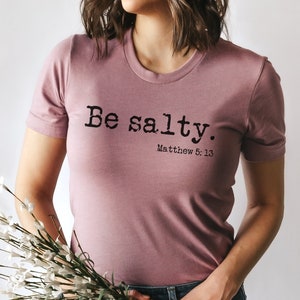 May include: A mauve t-shirt with the text "Be salty. Matthew 5:13" printed in black.