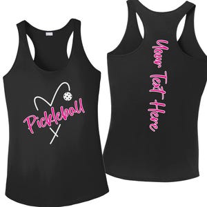 May include: Black tank top with a white heart and pickleball graphic. The word "Pickleball" is written in pink script. The back of the tank top has the text "Your Text Here" in pink script.