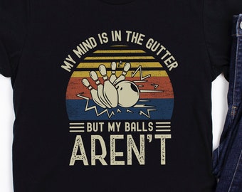 May include: Black t-shirt with a vintage-style graphic of bowling pins and a ball in a sunset. The text reads "My mind is in the gutter but my balls aren't".
