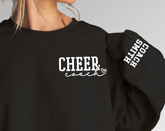 Pode incluir: Camisola de moletom preta com texto branco que diz "CHEER coach" na frente e "COACH SMITH" na manga.