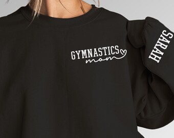 May include: Black sweatshirt with white text that says "Gymnastics Mom" with a heart symbol. The right sleeve has white text that says "Sarah".