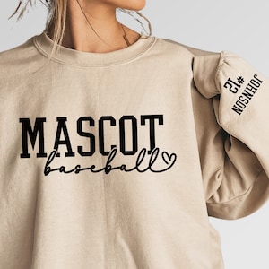 May include: A beige sweatshirt with black text that reads "MASCOT baseball" with a small heart symbol. The right sleeve has black text that reads "21# NOSNHEOC"