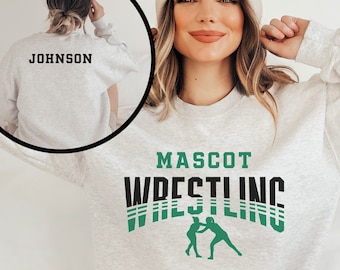 May include: Light gray sweatshirt with the text "MASCOT WRESTLING" in black and green. A silhouette of two wrestlers is below the text. The back of the sweatshirt has the name "JOHNSON" printed in black.