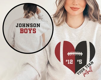 May include: Gray sweatshirt with a red and black heart-shaped football design. The heart has the numbers "#12" and "#5" on it. The text "YOUR TEAM Football" is written below the heart. The back of the sweatshirt has the text "JOHNSON BOYS" in red.