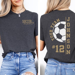 May include: A dark gray t-shirt with the text "Soccer Mom" on the front and the text "Your Team #12 Johnson" with a soccer ball graphic on the back.