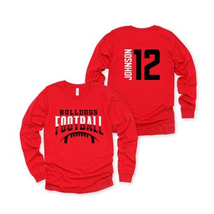 May include: Red long-sleeve t-shirt with a black and white football graphic and the text "Bulldogs Football". The back of the shirt has a black number "12" and the text "Johnson" in white.