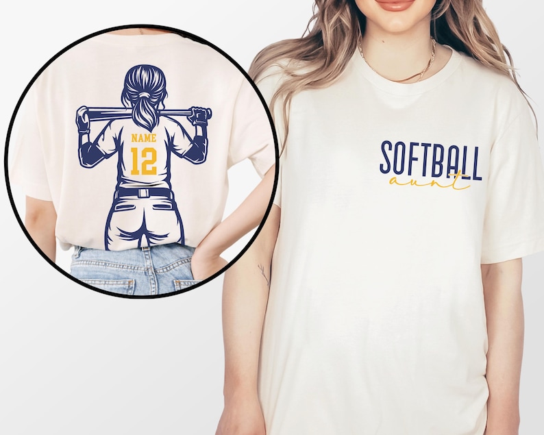 Puede incluir: Camiseta color crema con la frase "SOFTBALL aunt" en azul marino y amarillo. La parte trasera de la camiseta presenta un gr&aacute;fico de jugadora de softbol con un bate, el n&uacute;mero 12 y espacio para un nombre. El dise&ntilde;o es en azul marino y amarillo.
