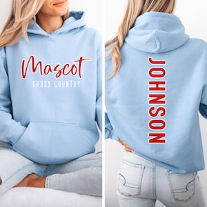 May include: Light blue hoodie with a front kangaroo pocket. The front features the word "Mascot" in red script above "Cross Country" in white. The back displays the name "JOHNSON" in red, vertically down the center.