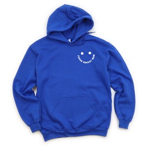 Peut inclure: Sweat-shirt &agrave; capuche bleu royal avec un graphique de visage souriant blanc qui dit "Proud Hockey Mom".