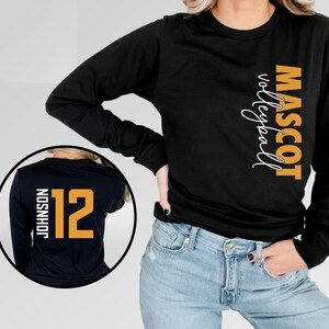 May include: Black long-sleeve shirt with the text "MASCOT volleyball" in orange on the right side. The back of the shirt has a white number "12" and the text "JOHNSON" in orange.
