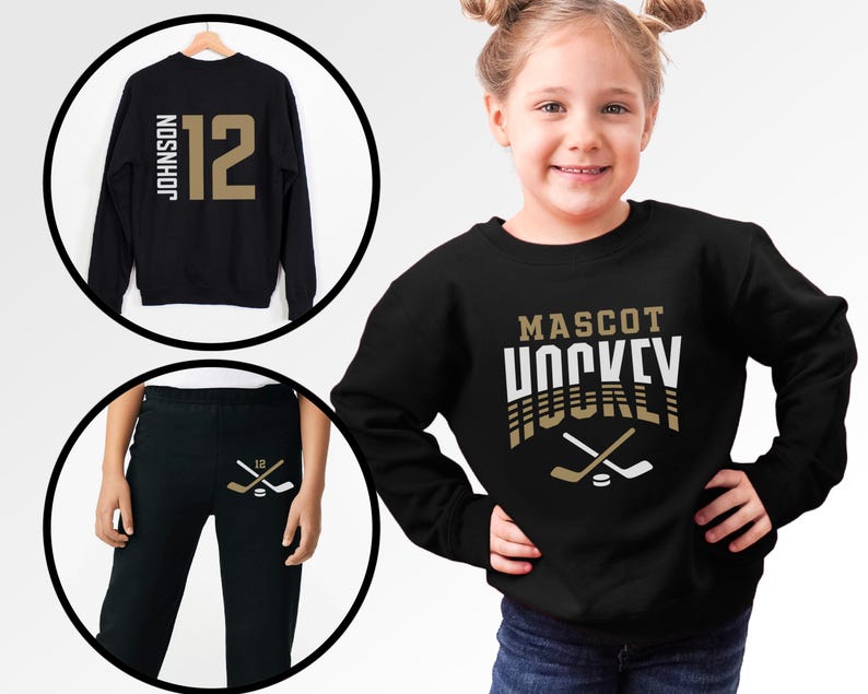 K&ouml;nnte beinhalten: Schwarzer Pullover mit dem Text "MASCOT HOCKEY" in goldenen und wei&szlig;en Buchstaben. Der Pullover hat ein Design mit gekreuzten Hockeyschl&auml;gern und einem Puck. Ein schwarzer Pullover mit der Nummer "12" und dem Namen "JOHNSON" in goldenen Buchstaben. Schwarze Jogginghose mit einem Hockeyschl&auml;ger- und Puck-Design in Gold.