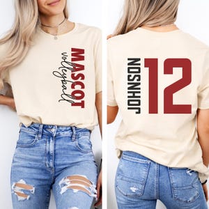 May include: A beige t-shirt with the text "MASCOT volleyball" printed vertically on the front and the text "JOHNSON 12" printed vertically on the back.