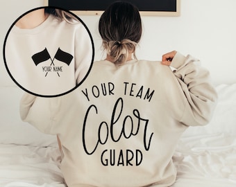 May include: A beige sweatshirt with the text "YOUR TEAM Color GUARD" printed on the back. The front of the sweatshirt has two crossed flags with the text "YOUR NAME" underneath.