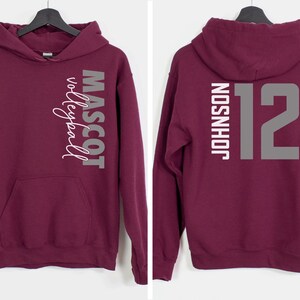 May include: Burgundy hooded sweatshirt with a white graphic on the left side that says "Mascot Volleyball" and a white graphic on the right side that says "Johnson 12".