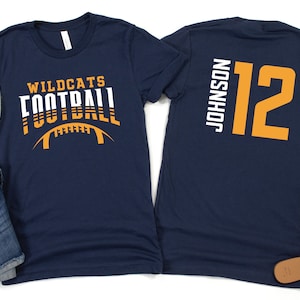 May include: Two navy blue t-shirts. The front of one shirt has the text "Wildcats Football" in white and orange. The back of the other shirt has the text "Johnson 12" in white and orange.