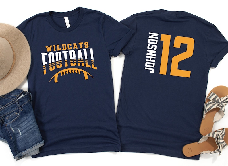 May include: Two navy blue t-shirts. The front of one shirt has the text "Wildcats Football" in white and orange. The back of the other shirt has the text "Johnson 12" in white and orange.
