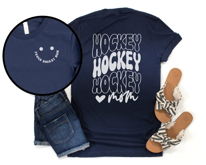 Peut inclure: T-shirt bleu marine avec un motif blanc qui dit "Hockey Hockey Hockey Mom" avec un c&oelig;ur. Le devant du t-shirt a un smiley blanc avec le texte "Proud Hockey Mom".