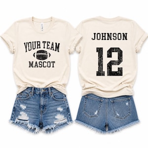 May include: Two cream-colored t-shirts and two pairs of blue denim shorts. The front of one shirt features the text "YOUR TEAM MASCOT" with a football graphic. The back of the other shirt displays the name "JOHNSON" above the number "12".