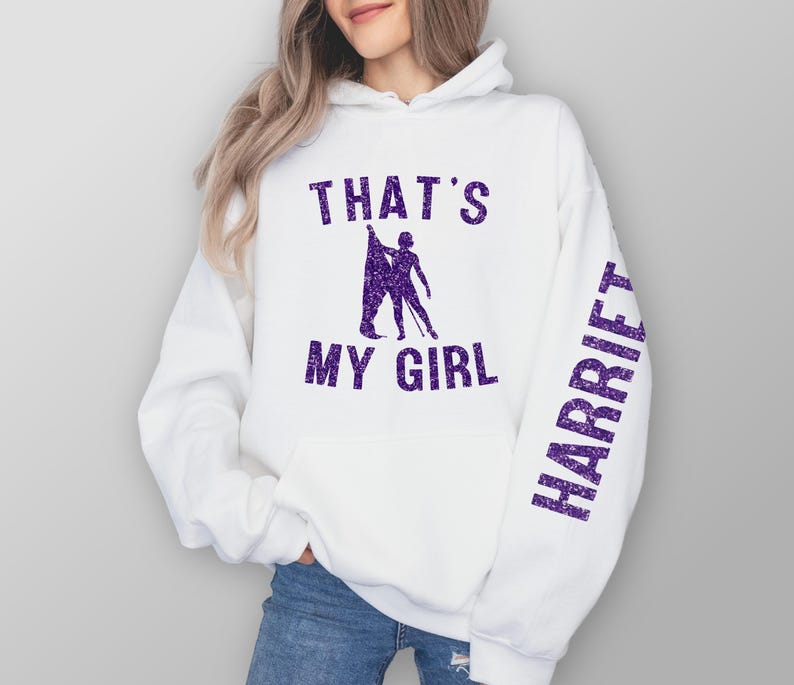 May include: White hoodie with purple glitter text that says "That's My Girl" and "Harriett" on the sleeve.