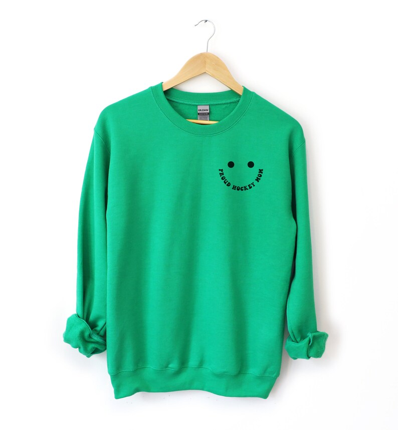 Peut inclure: Sweat-shirt vert avec un smiley noir et le texte "Proud Hockey Mom" sur le devant.