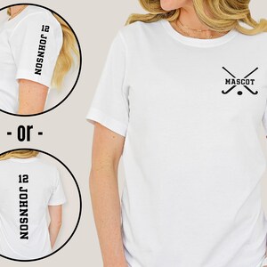 May include: White t-shirt with a black hockey stick graphic and the word "MASCOT" on the front. The back of the shirt has the number "12" and the word "JOHNSON" printed vertically.