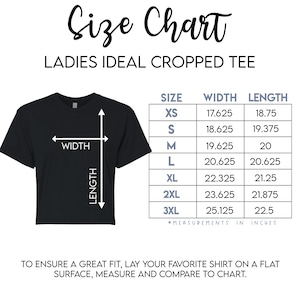 Pu&ograve; includere: T-shirt nero cropped con tabella taglie. La tabella elenca le taglie XS-3XL con misure di larghezza e lunghezza in pollici. Il testo "Size Chart" e "LADIES IDEAL CROPPED TEE" sono in alto.