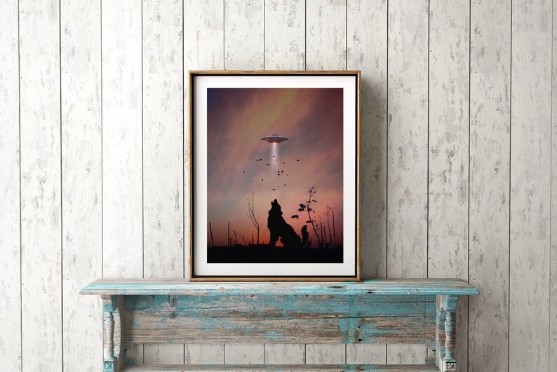 K&ouml;nnte beinhalten: Ein gerahmter Druck eines Wolfes, der zu einem UFO am Himmel heult. Der Wolf ist vor einem Sonnenuntergangshimmel mit ein paar V&ouml;geln, die herumfliegen, silhouettiert.