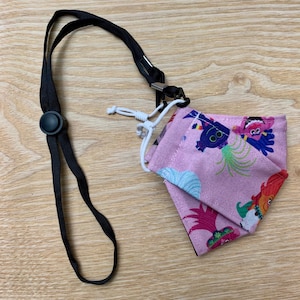 May include: A pink face mask with a colorful cartoon print of characters. The mask is attached to a black lanyard with a plastic clasp.
