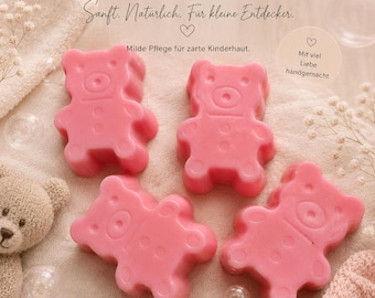 May include: Four pink bear-shaped soaps arranged on a textured surface. The text reads: KLEINE TEDDYS, Sanft. Natürlich. Für kleine Entdecker., Milde Pflege für zarte Kinderhaut., Mit viel Liebe handgemacht, Hintergrund digital erstellt – Produkt 100 % handgemacht.
