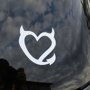 May include: White vinyl decal of a heart with devil horns on a black car window.
