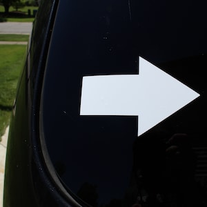 May include: A white arrow sticker on a black car window. The arrow points to the right.