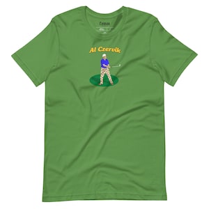 May include: Green short-sleeved t-shirt with the text "Al Czervik" in yellow and a cartoon illustration of a golfer wearing a blue shirt and red and white patterned pants.