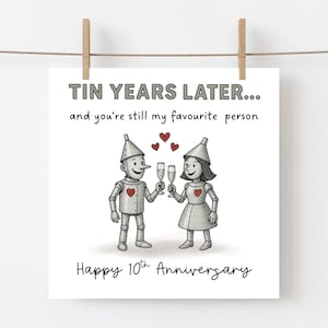 K&ouml;nnte beinhalten: Eine quadratische Gru&szlig;karte mit zwei silbernen Zinnfiguren, die mit Champagnergl&auml;sern ansto&szlig;en. Der Text lautet: TIN YEARS LATER... and you're still my favourite person. Happy 10th Anniversary. Drei kleine rote Herzen schweben &uuml;ber den Figuren.