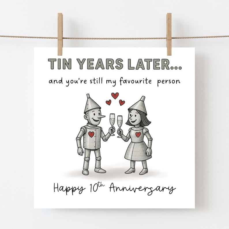 K&ouml;nnte beinhalten: Eine quadratische Gru&szlig;karte mit zwei silbernen Zinnfiguren, die mit Champagnergl&auml;sern ansto&szlig;en. Der Text lautet: TIN YEARS LATER... and you're still my favourite person. Happy 10th Anniversary. Drei kleine rote Herzen schweben &uuml;ber den Figuren.