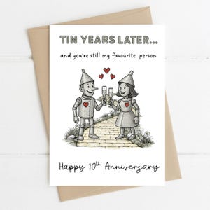 Könnte beinhalten: Eine Grußkarte mit braunem Umschlag. Die Karte zeigt einen Blechmann und eine Blechfrau, die mit Champagnergläsern anstoßen. Der Text lautet: "Tin Years Later... and you're still my favourite person. Happy 10th Anniversary."