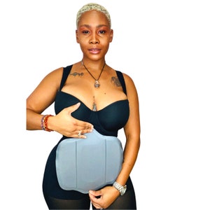 May include: A woman wearing a black bra and a gray compression garment with a panel design. The garment is designed to help support the abdomen and back.