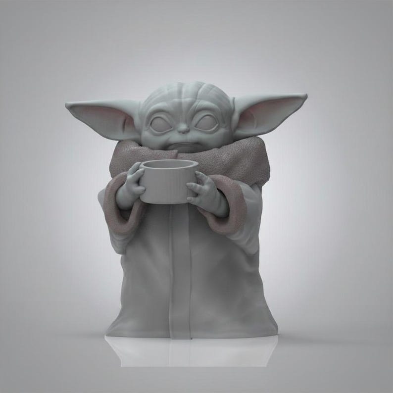 K&ouml;nnte beinhalten: Graue Figur einer Figur aus einem beliebten Science-Fiction-Franchise, die eine kleine Tasse h&auml;lt. Die Figur hat gro&szlig;e Ohren, eine zerknitterte Stirn und tr&auml;gt eine Robe mit einem fellartigen Kragen. Die Figur steht auf einer wei&szlig;en Oberfl&auml;che.