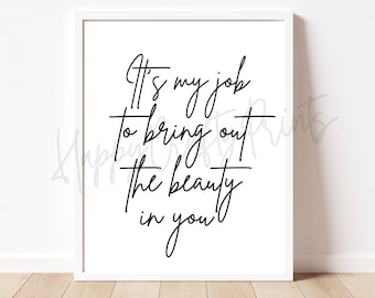 May include: A framed white print with black cursive text that reads, "It's my job to bring out the beauty in you." The print is displayed against a white wall.