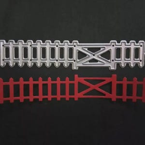 May include: Two metal fence die cuts. The top die cut is silver and the bottom die cut is red. Both have a gate design in the center. The silver die cut has a more detailed design than the red die cut.