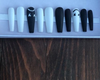 May include: A set of ten false nails, five black and five white. The black nails have a white smiley face with an 'X' for eyes.