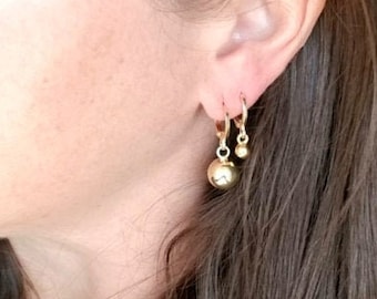 May include: A person wearing gold hoop earrings with a dangling ball charm.