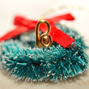 Peut inclure: Une petite couronne de Noël de couleur bleu sarcelle avec un ruban rouge et une décoration en métal doré en forme de lettre B.