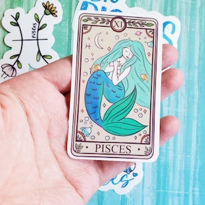 May include: A sticker featuring a mermaid with a blue and green tail, surrounded by stars and bubbles. The sticker has the text "Pisces" and the number "XI" on it.