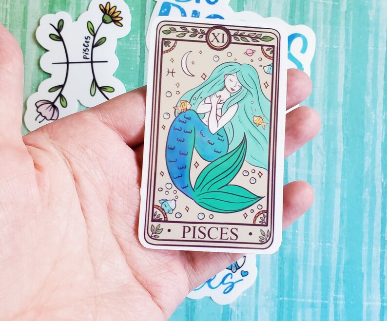 May include: A sticker featuring a mermaid with a blue and green tail, surrounded by stars and bubbles. The sticker has the text "Pisces" and the number "XI" on it.