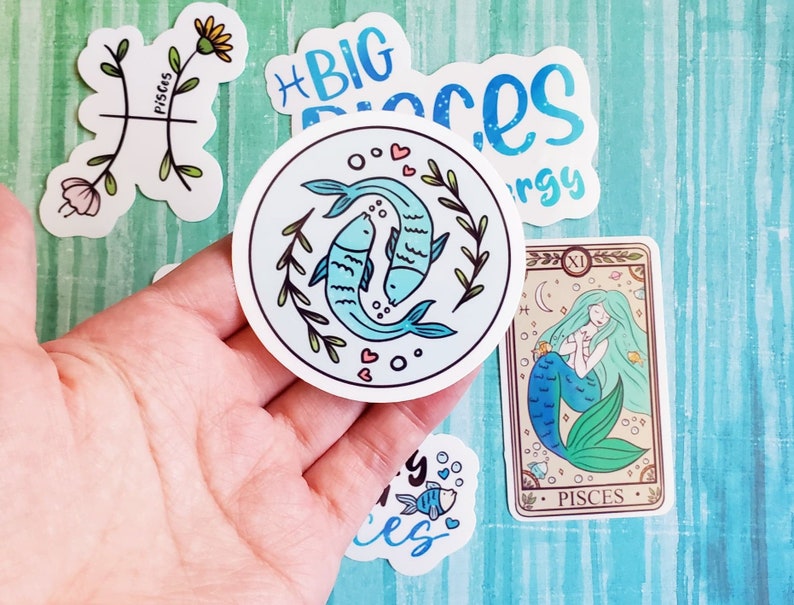 May include: A set of five stickers featuring the astrological sign Pisces. The stickers are round and feature a variety of designs, including two fish swimming, a mermaid, and the word "Pisces".